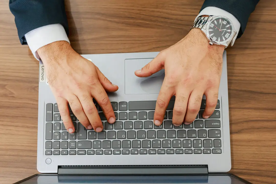 Manos escribiendo en una laptop sobre un escritorio de madera